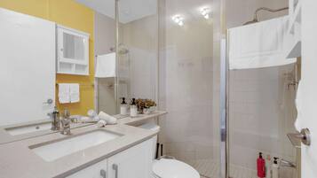 A modern bathroom with a glass shower enclosure, a white toilet, and a vanity with a sink and mirror.