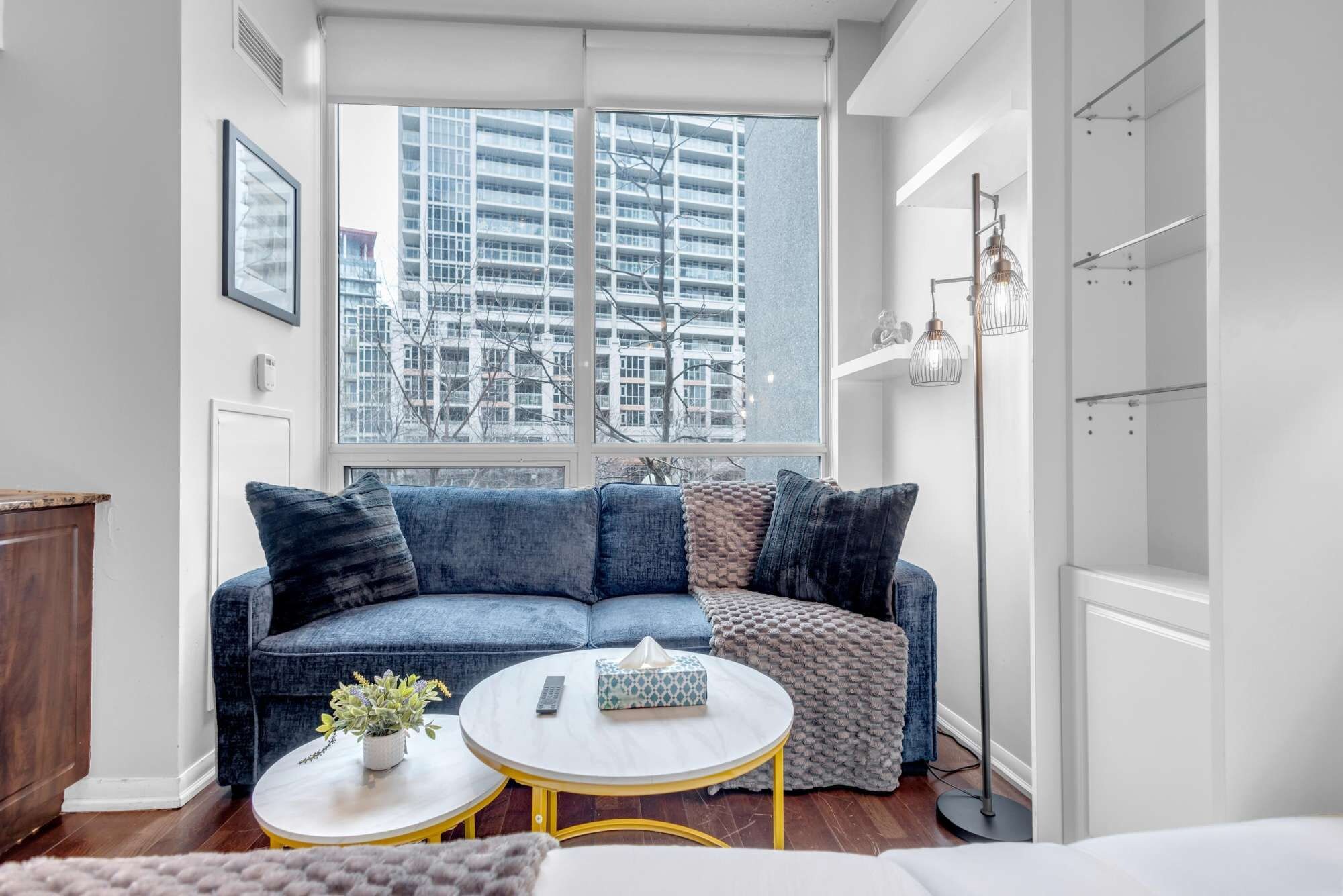 A modern living room with a large window, a blue sofa, a round coffee table, and a floor lamp.