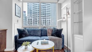 A modern living room with a large window, a blue sofa, a round coffee table, and a floor lamp.