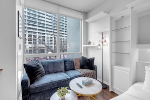 Ein modernes Wohnzimmer mit einer Couch, einem Couchtisch und Blick auf eine Stadtkulisse durch große Fenster.