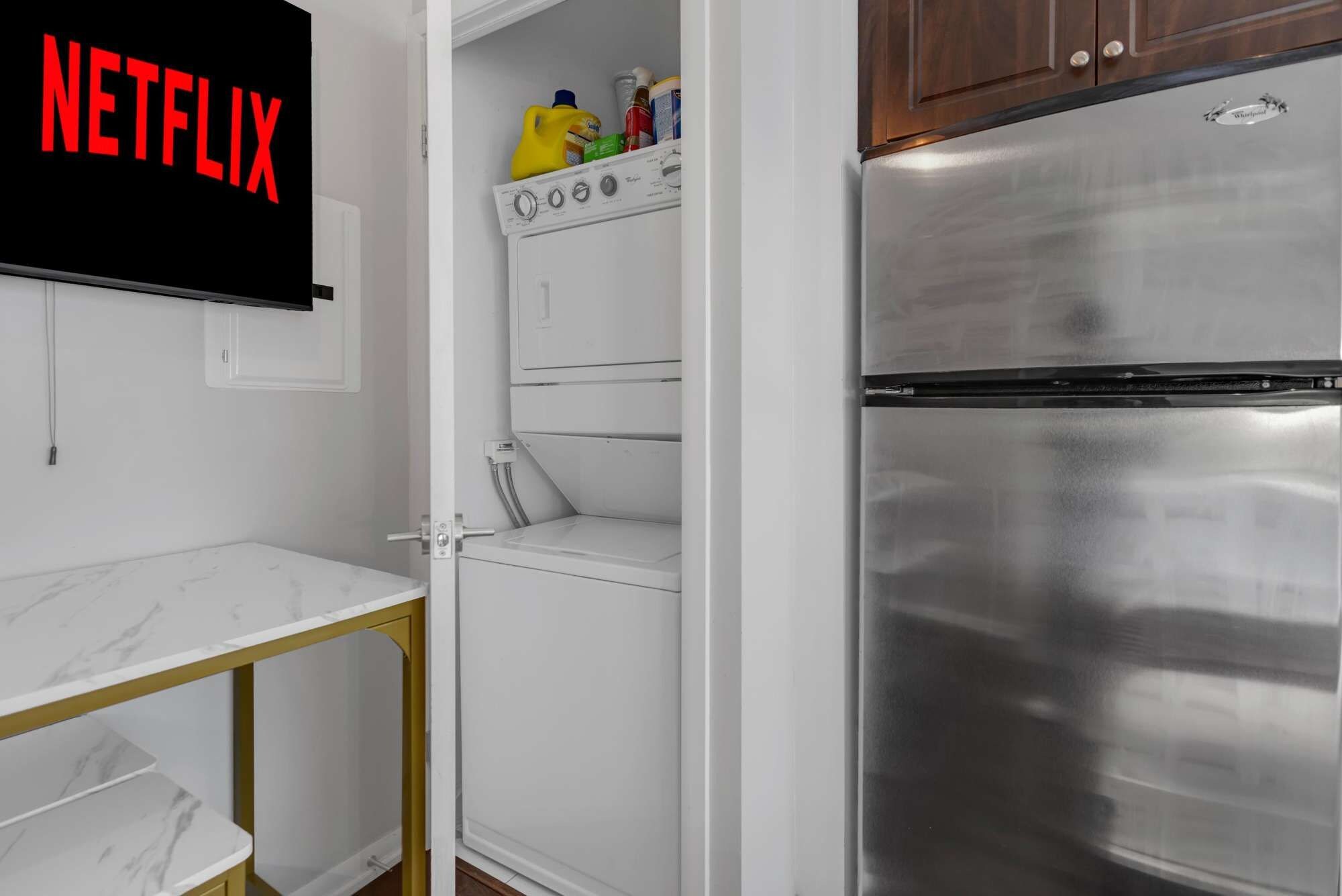 A compact kitchen with a stainless steel refrigerator, a washing machine, and a marble countertop.