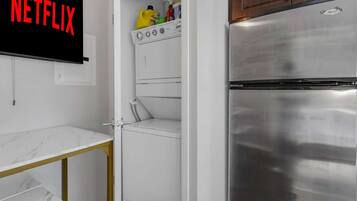 A compact kitchen with a stainless steel refrigerator, a washing machine, and a marble countertop.