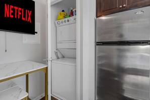 Une cuisine compacte dotée d’un réfrigérateur en acier inoxydable, d’un lave-linge et d’un plan de travail en marbre.