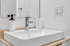 Ein weißes Waschbecken mit chromfarbenem Wasserhahn, eine Handseifenflasche und ein Handtuchhalter mit zwei weißen Handtüchern.