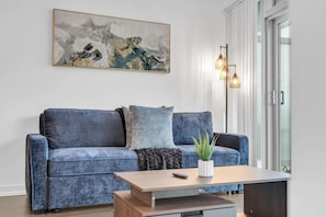 Ein Wohnzimmer mit einem blauen Sofa, einem Couchtisch, einer Pflanze und einem Bild an der Wand.