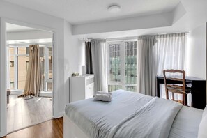 Ein Hotelzimmer mit Bett, Schreibtisch und Stuhl. Ein Fenster mit Vorhängen und eine Tür zu einem weiteren Raum.
