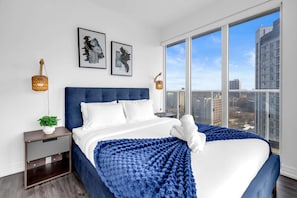 Une chambre à coucher moderne avec un grand lit, une table de chevet, une plante en pot et deux lampes fixées au mur.