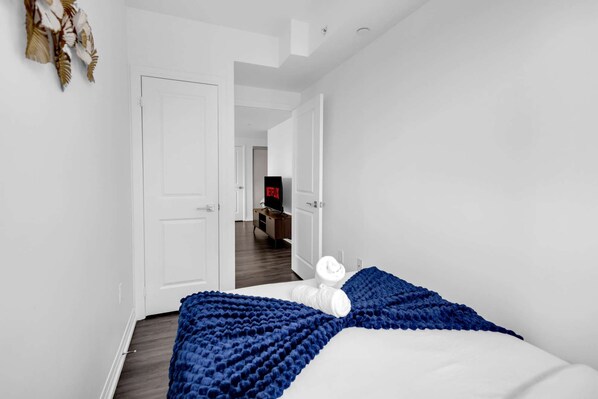 Une chambre d’hôtel avec un lit, une porte blanche, un couloir et un téléviseur à l’arrière-plan.