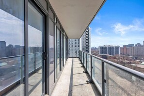 Un balcon avec vue sur la ville, doté de rampes en verre et d’un sol en béton.