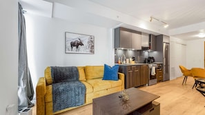 A modern living room with a sofa, a coffee table, and a kitchen area with cabinets and appliances.