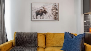 A room with a sofa, a framed picture of a moose, and a window with blinds. - RivetStays | The Jarvis Executive Suite – 2 Bedroom Suite (Toronto)