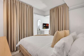 Une chambre d’hôtel avec un grand lit, des rideaux, une télévision et une salle de bain visible à travers une porte ouverte.