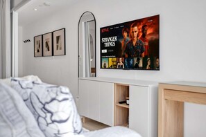Une chambre moderne dotée d’un grand téléviseur à écran plat fixé au mur, qui affiche l’interface de Netflix.