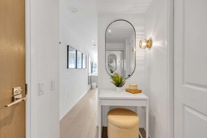 Un couloir avec un mur blanc, un miroir, une petite table avec une plante et un banc.