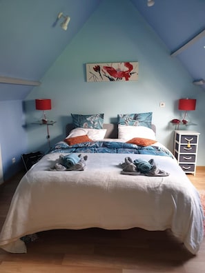 Ein Schlafzimmer mit schrägen Wänden, einem Bett mit weißer Bettdecke, mehreren Kissen und zwei Nachttischen mit Lampen.