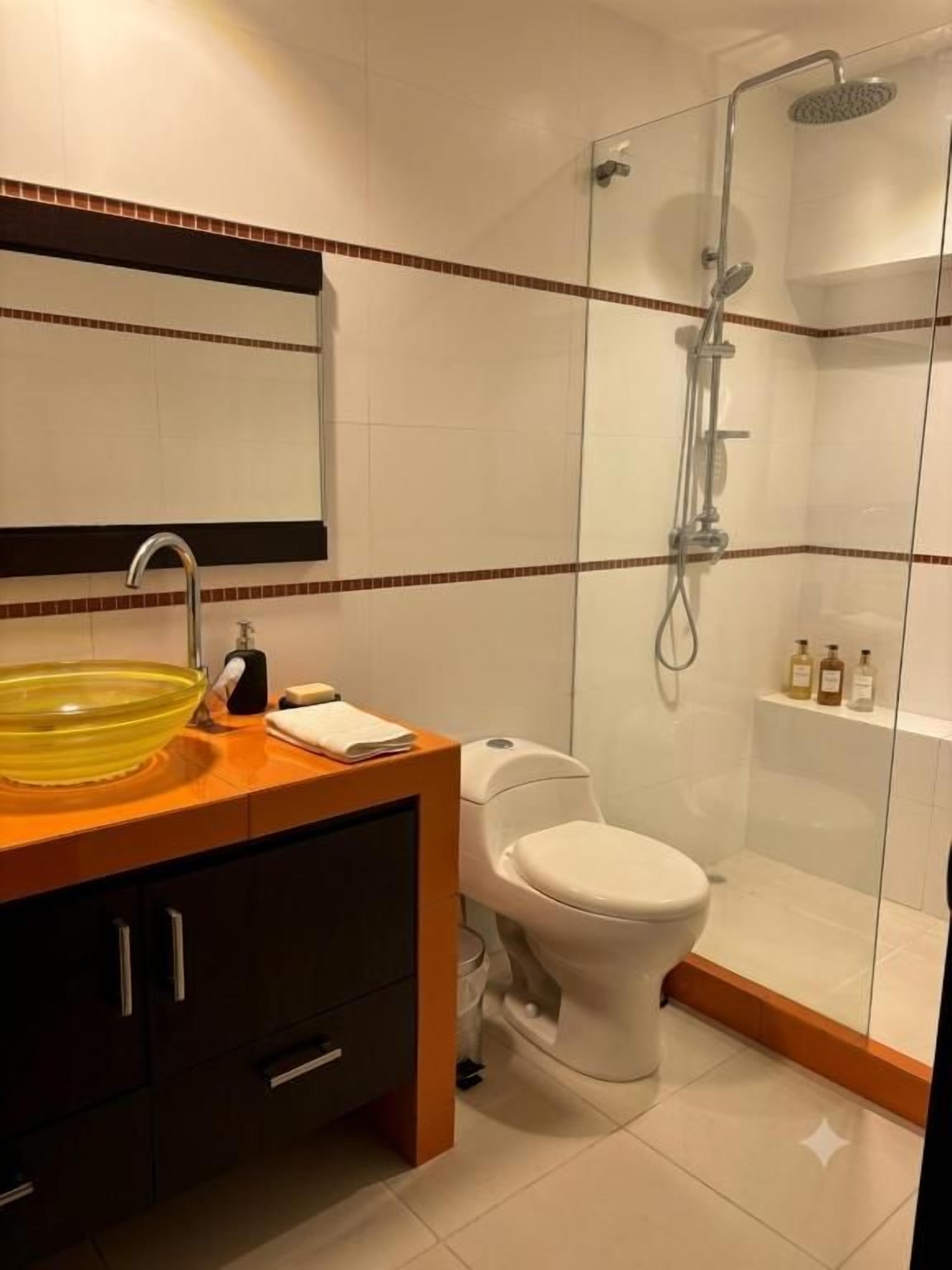 Un baño moderno con ducha envuelta en vidrio, inodoro blanco y tocador de madera con lavabo de cristal.
