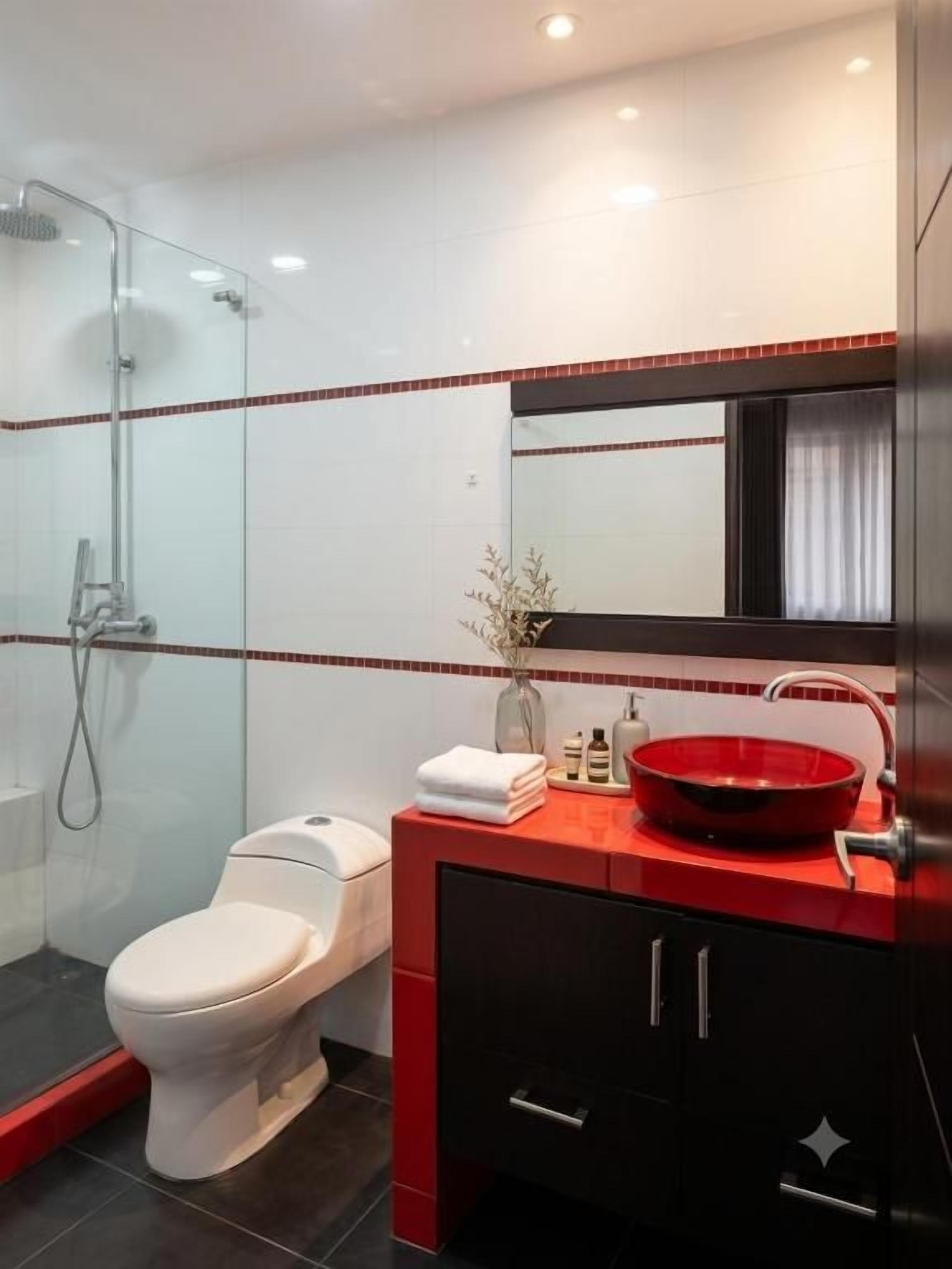 Ein modernes Badezimmer mit einer Duschkabine aus Glas, einer weißen Toilette, einem roten Waschbecken und einem schwarzen Schrank.