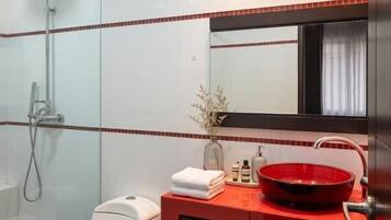 Ein modernes Badezimmer mit einer Duschkabine aus Glas, einer weißen Toilette, einem roten Waschbecken und einem schwarzen Schrank.