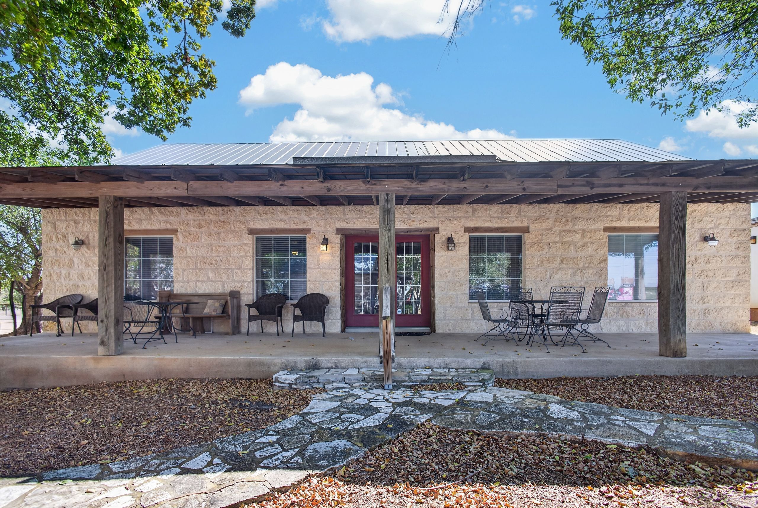 A building with a stone facade, a red door, and a covered patio area with outdoor seating.
