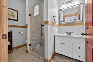 Ein Badezimmer mit Duschkabine aus Glas, einem weißen Waschbecken mit Spiegel darüber und einem Holztürrahmen.