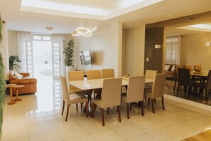 A modern dining area with a large table and chairs, a sofa, and a television.