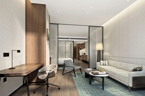 Una habitación de hotel moderna con escritorio, dos sillas, un sofá, una mesita y una lámpara.