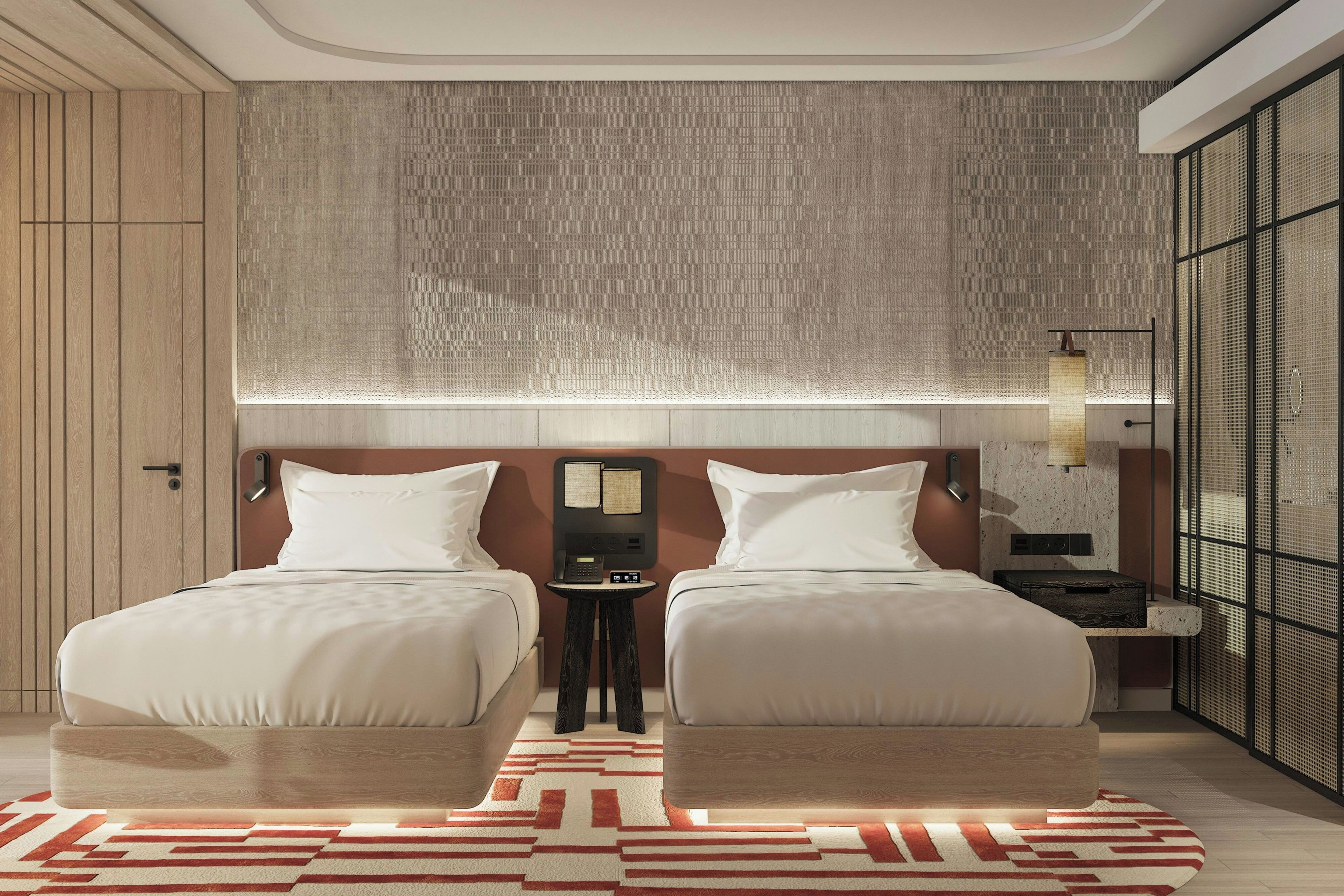 Ein Hotelzimmer mit zwei Betten, einem kleinen Nachttisch, einem an der Wand befestigten Telefon und einem gemusterten Teppich.