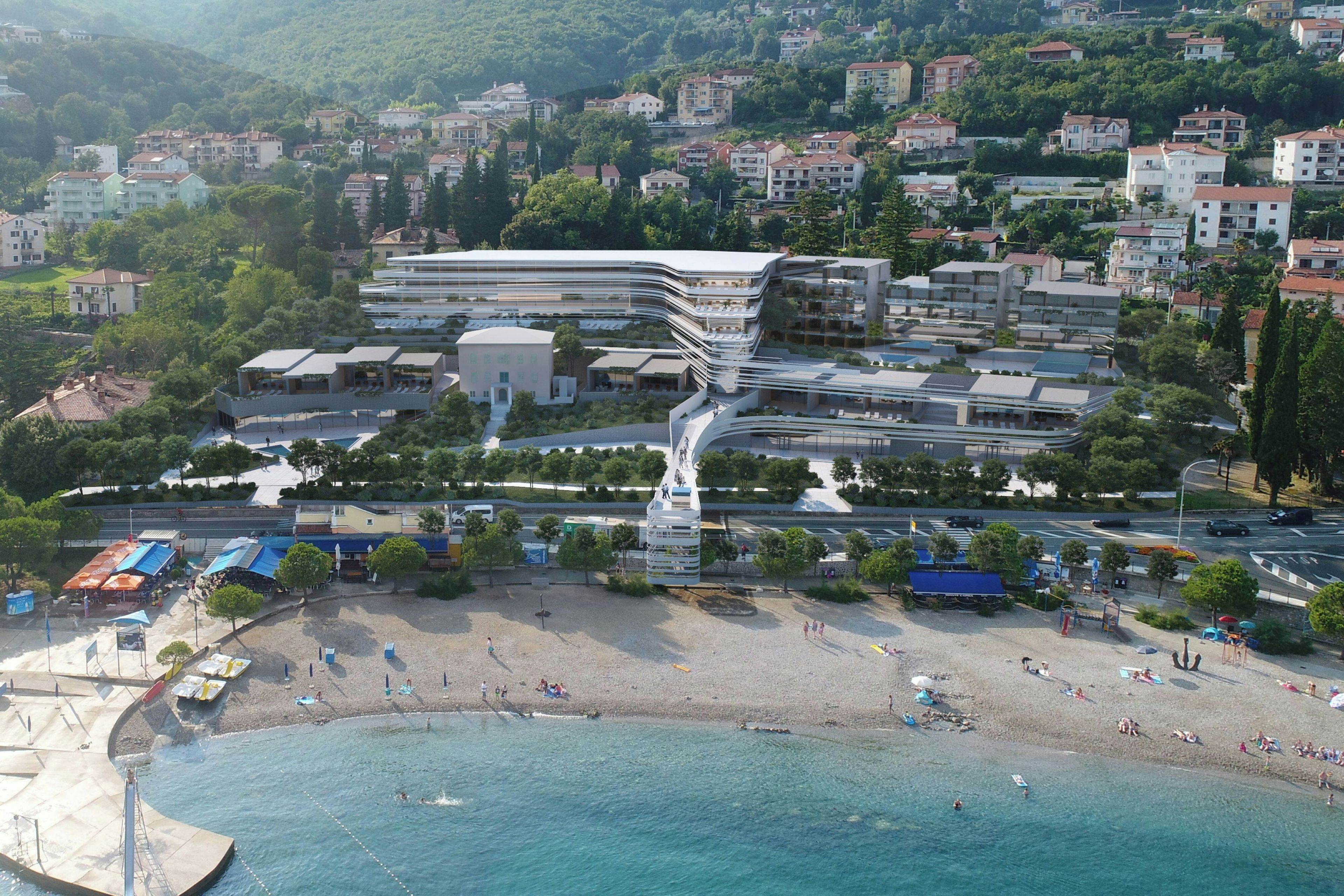 Eine Küstenlandschaft mit einem modernen Gebäudekomplex, einem Strand und Wohnhäusern im Hintergrund.