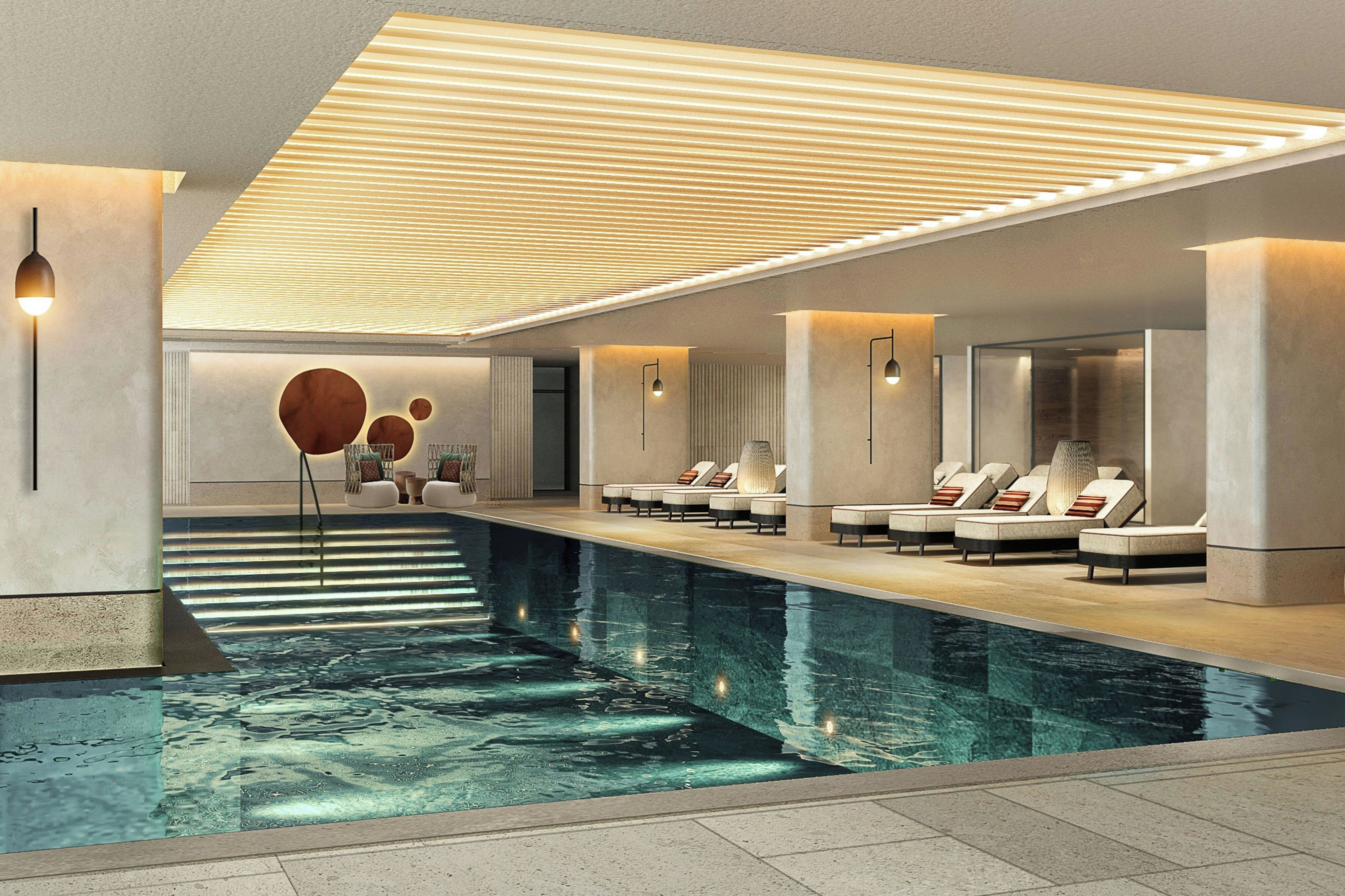 Un espace piscine intérieur moderne, doté de chaises longues et d’un plafond orné de luminaires linéaires.