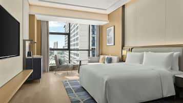 A hotel room with a large bed, a desk, a chair, a TV, and a view of the city.