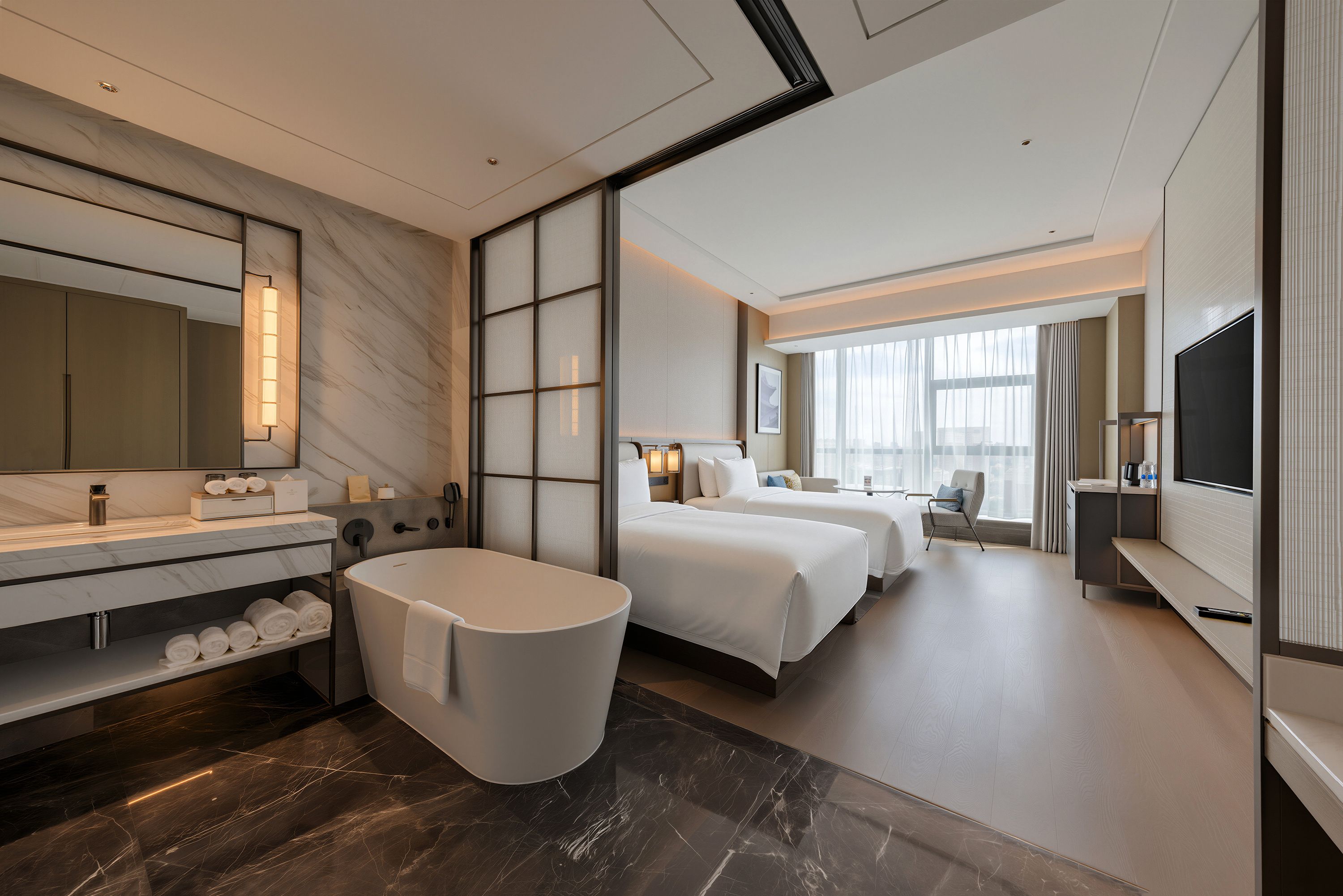 Habitación de hotel moderna con una cama grande, zona de estar separada, bañera y televisor.