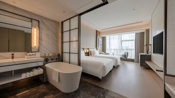 Habitación de hotel moderna con una cama grande, zona de estar separada, bañera y televisor.