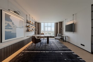 A modern living room with a dining area, a large window, and a flat-screen TV mounted on the wall.