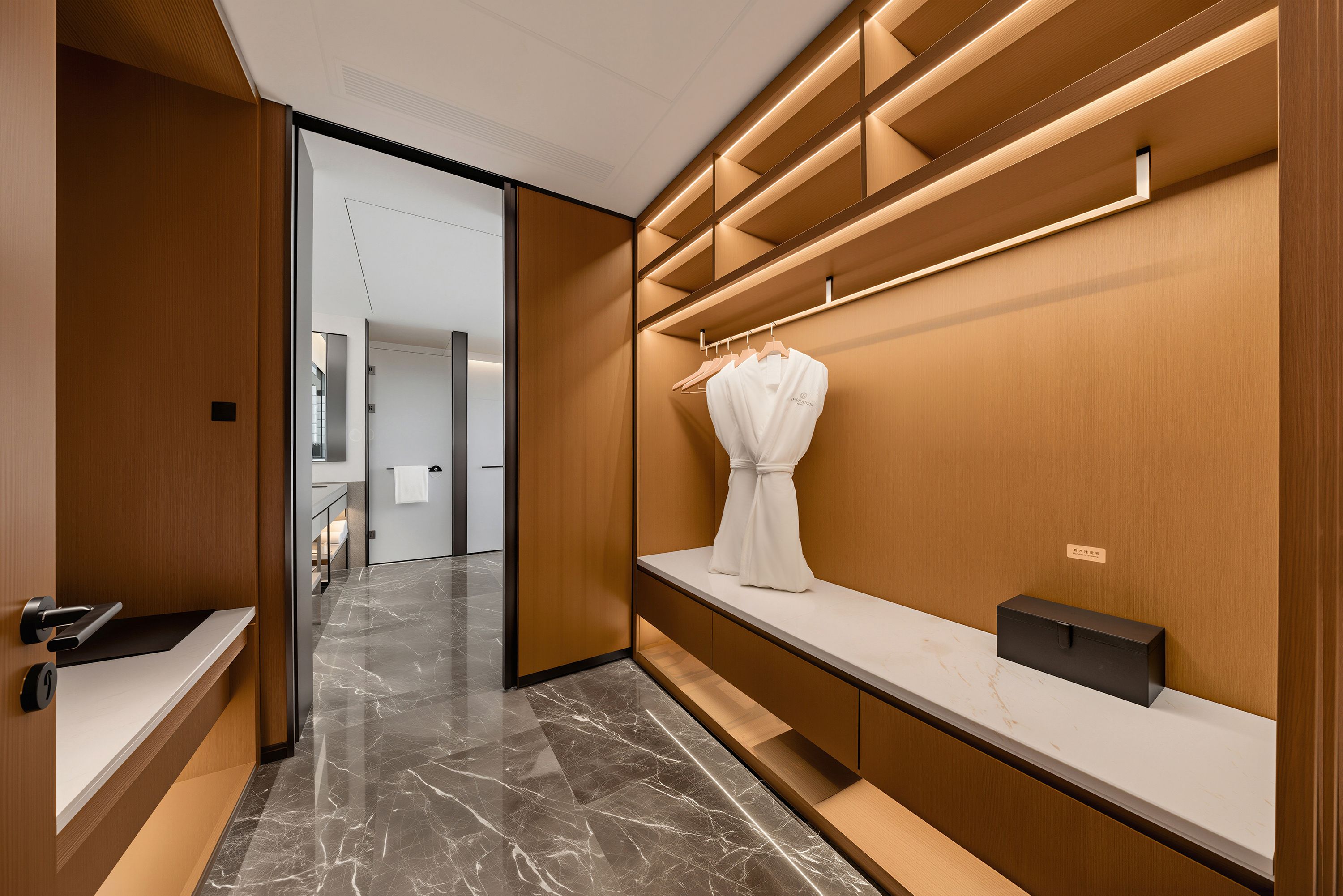 Ein moderner Hotelkorridor mit Marmorboden, Holzvertäfelung und einem Kleiderständer mit einem weißen Kleidungsstück.