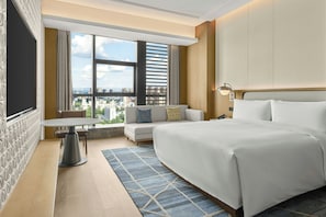 Habitación de hotel con cama, una pequeña mesa, sofá, ventana con vista a la ciudad y una alfombra estampada.
