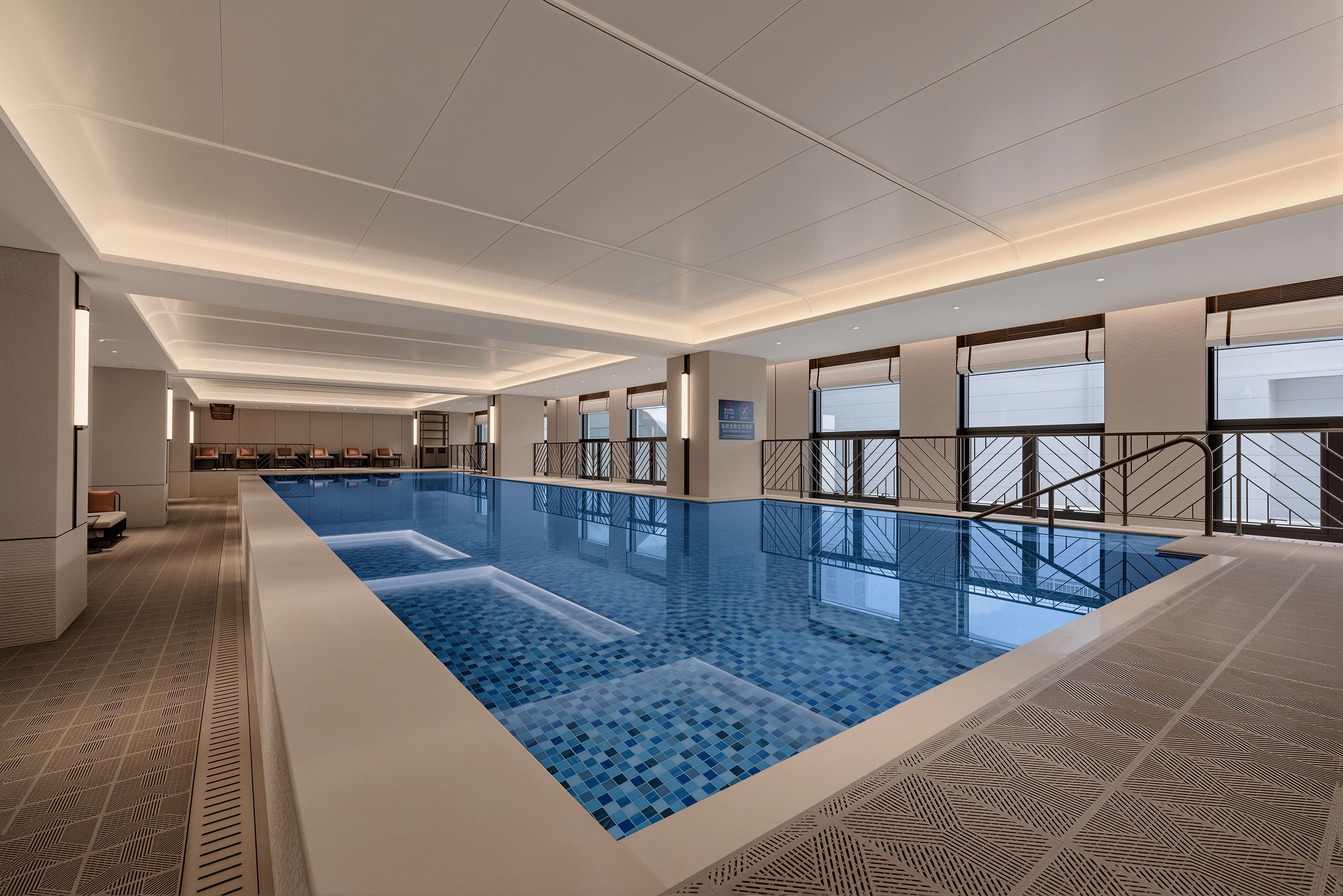 Una gran piscina interior con suelo de baldosas, rodeada de paredes con diseños decorativos y ventanas.
