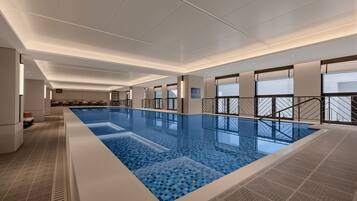 Una gran piscina interior con suelo de baldosas, rodeada de paredes con diseños decorativos y ventanas.