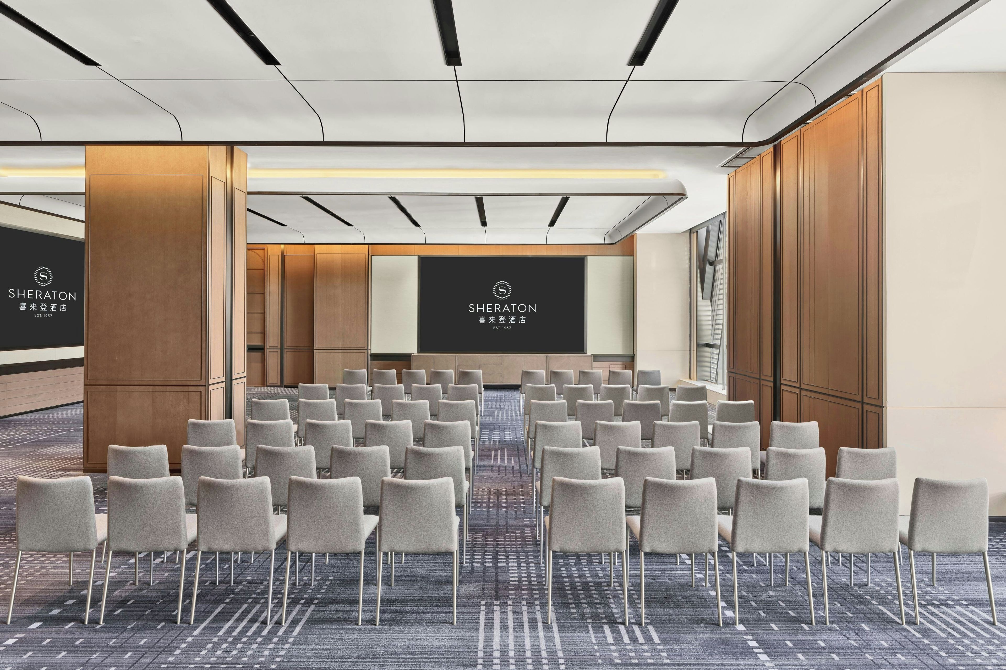 A conference room with rows of chairs, a large screen, and wooden paneling.