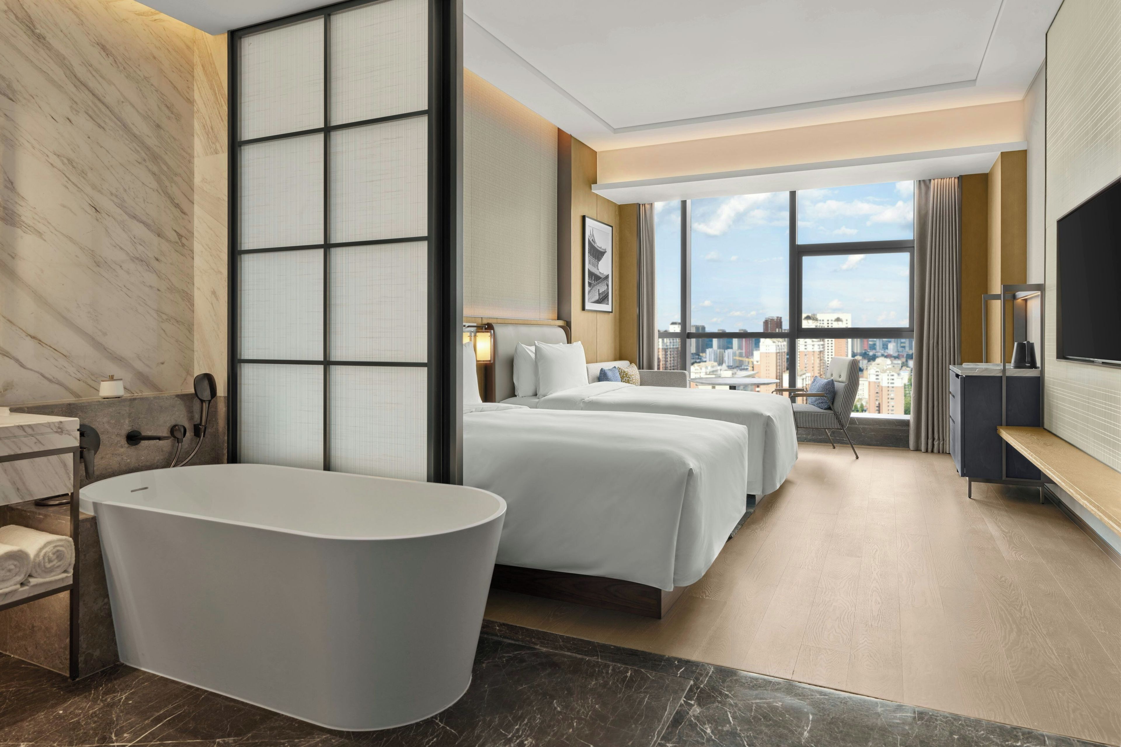 Habitación de hotel con un ventanal grande, una bañera, dos camas y un escritorio.