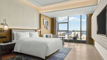 A hotel room with a large bed, a desk, a chair, a TV, and a city view.