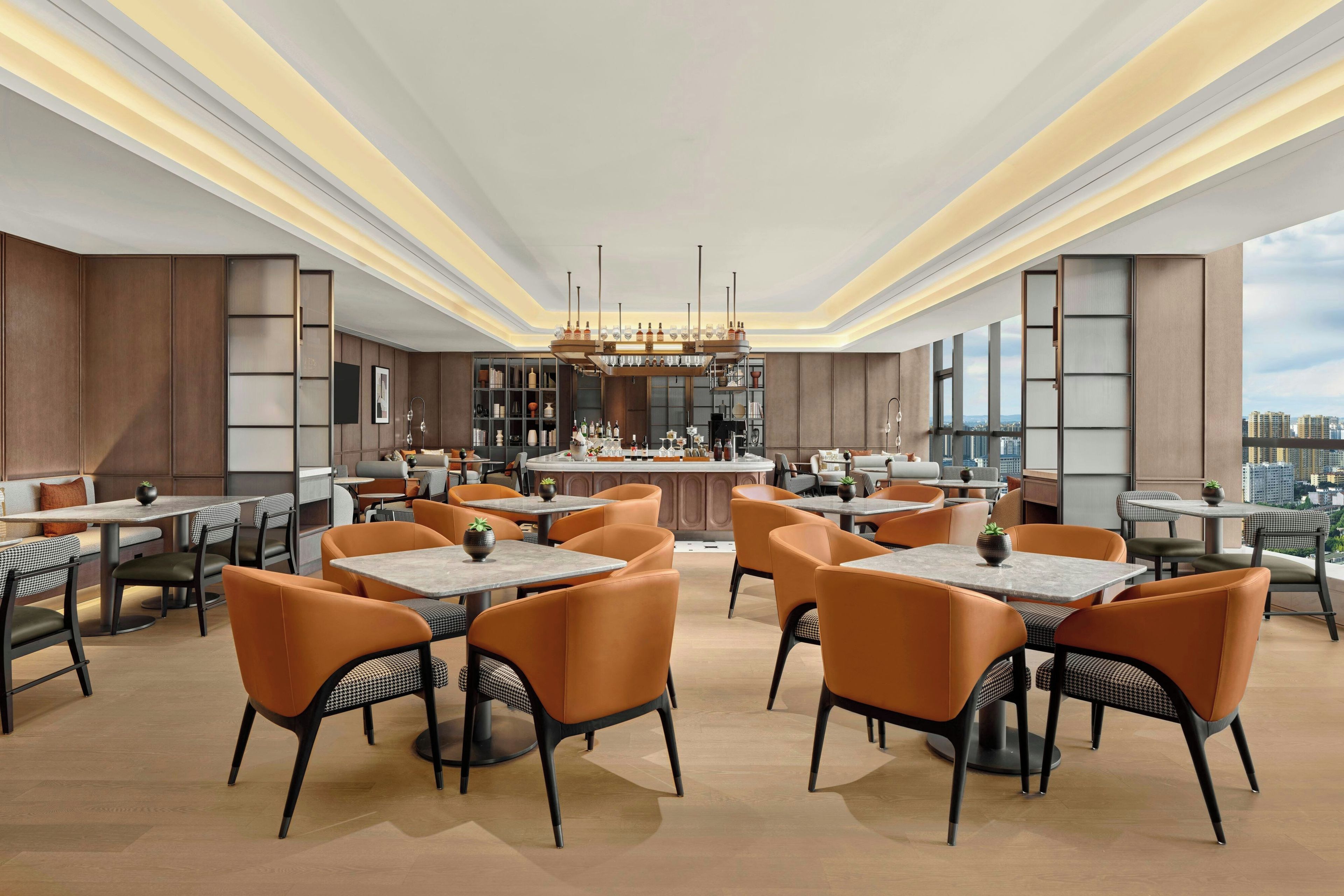 Un espace de restauration moderne doté de plusieurs tables et chaises, d’un bar central et offrant une vue sur la ville.
