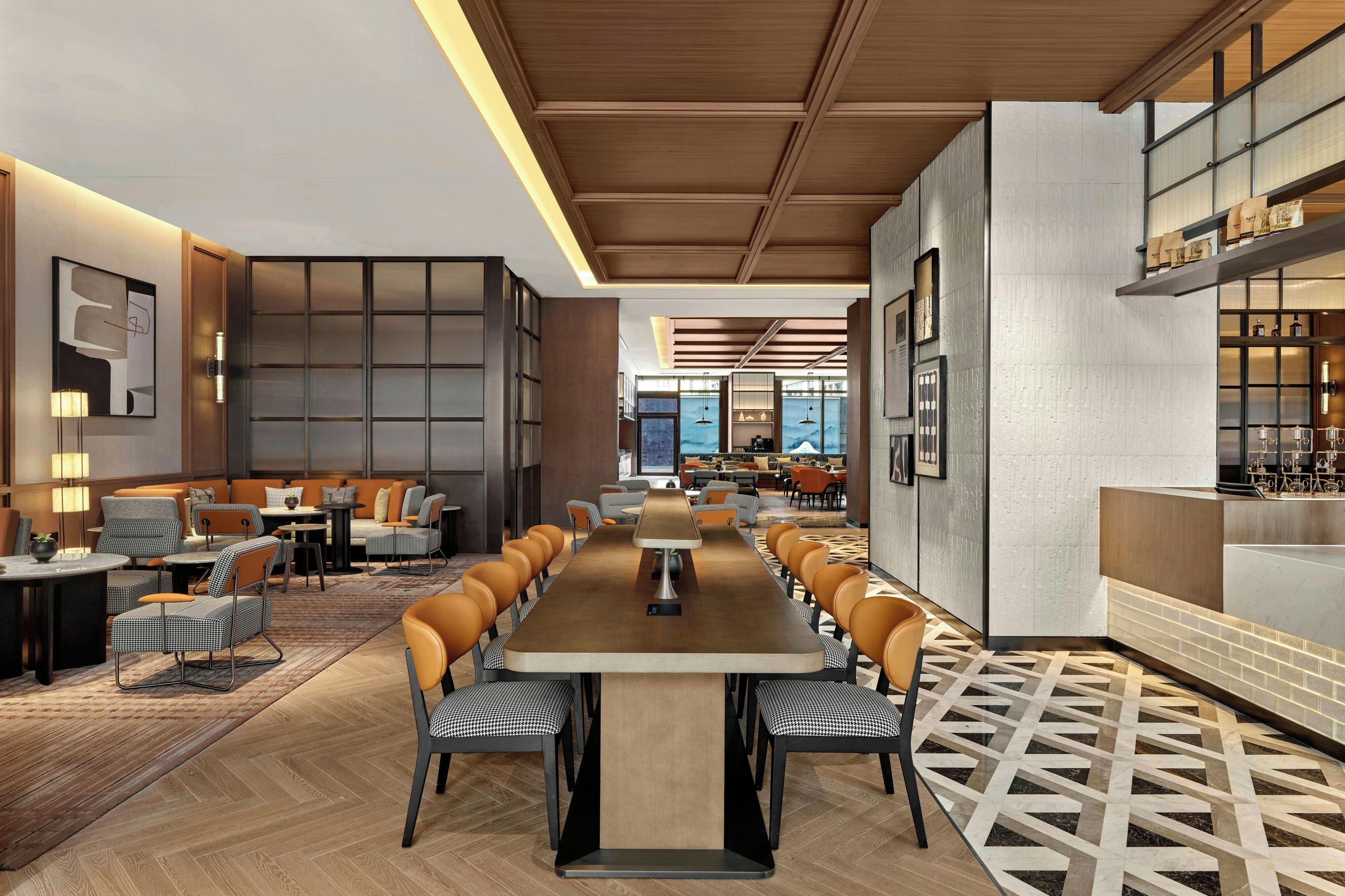 Un hall d’hôtel moderne avec une longue table commune, des espaces de détente et une vue sur le paysage urbain grâce à de grandes fenêtres.
