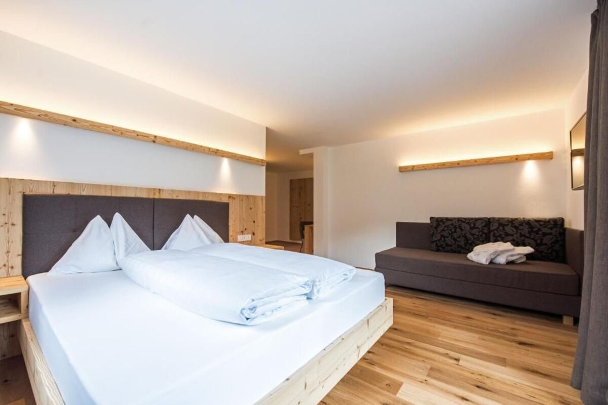 Une chambre d’hôtel avec un lit, un canapé, un plancher en bois et un éclairage intégré.