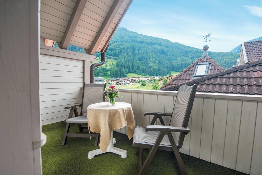 A balcony with a table and chairs, overlooking a village and mountains.