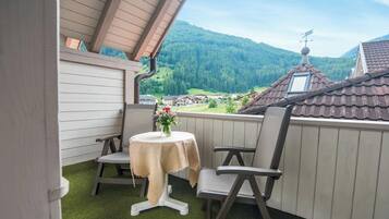 A balcony with a table and chairs, overlooking a village and mountains.