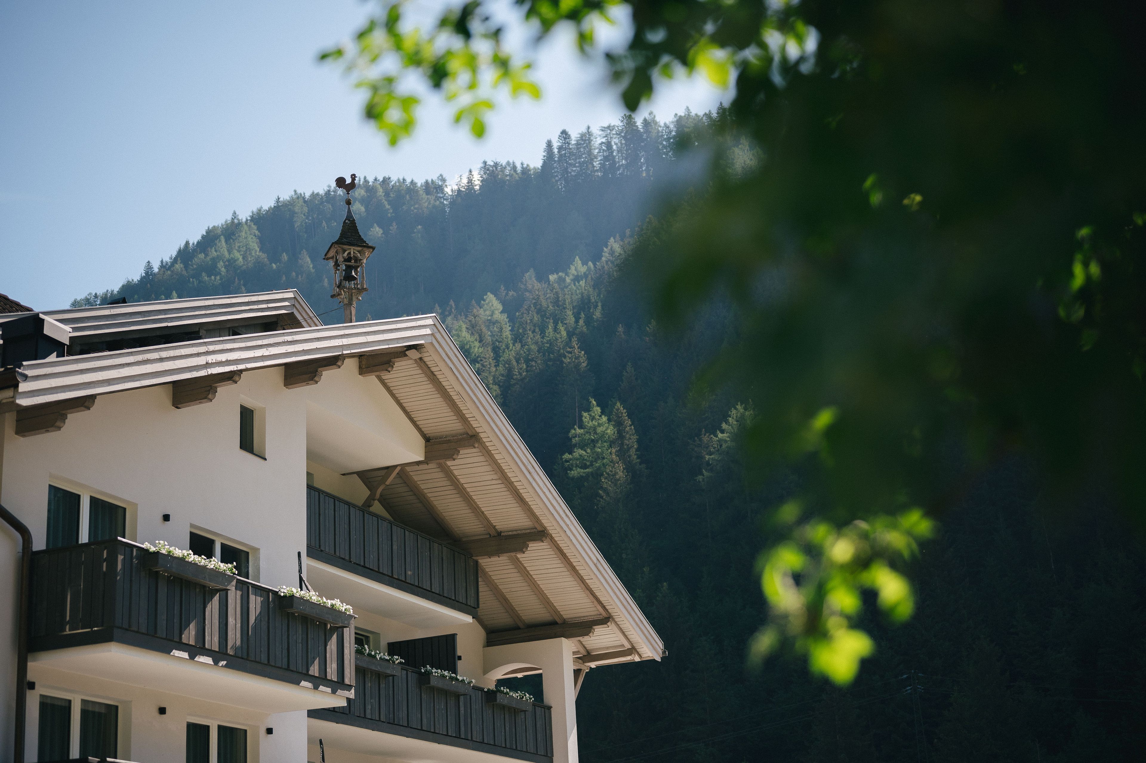 Ein Gebäude mit Balkon, einem Glockenturm und einem bewaldeten Hügel im Hintergrund.