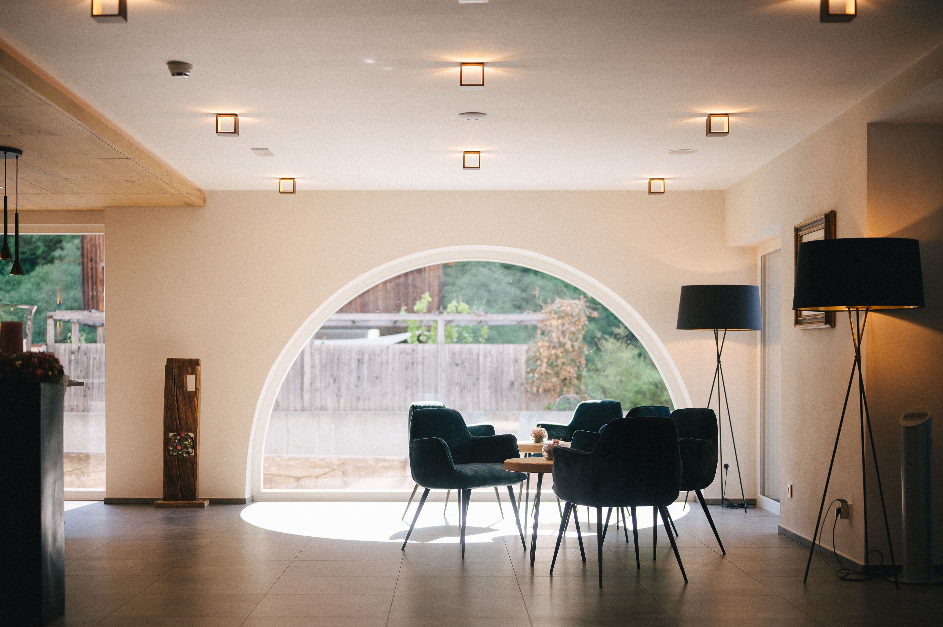 A modern interior with a large arched window, a dining area with chairs, and a floor lamp.