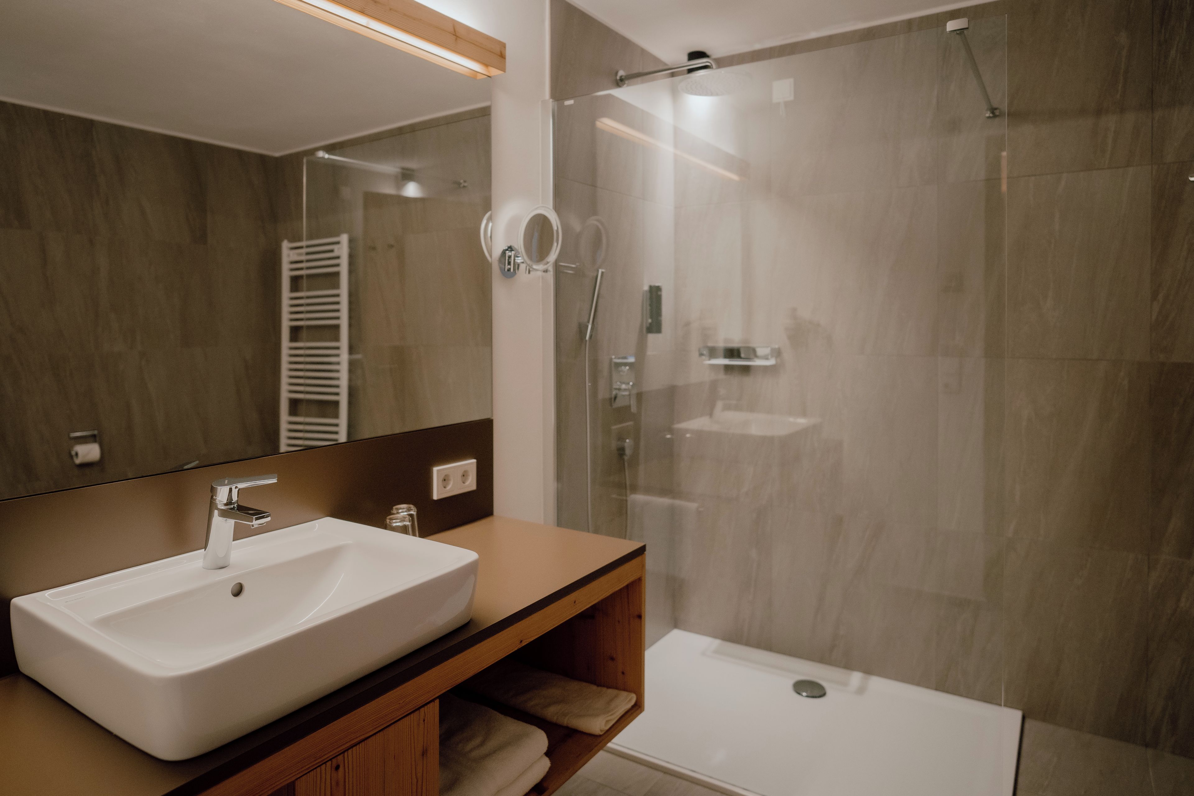A modern bathroom with a white sink, a glass shower enclosure, and a wooden vanity.