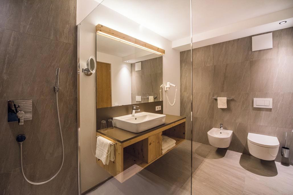 Un baño moderno con ducha envuelta en cristal, tocador de madera, espejo grande y un bidé.