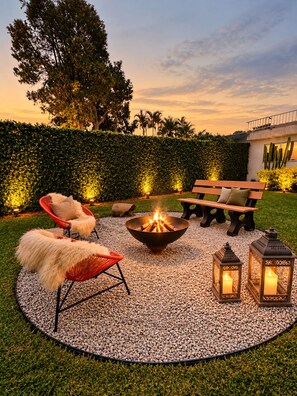 Un área de estar al aire libre con un brasero, sillones de descanso y faroles.